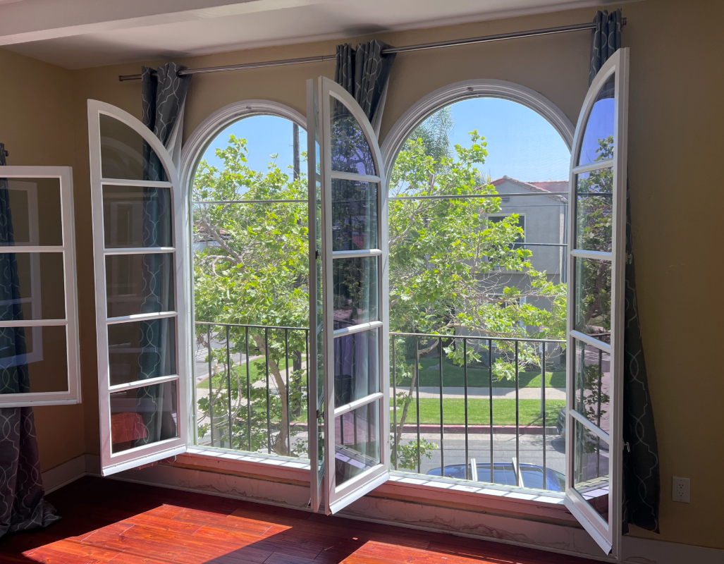 Open arched windows with white frames, overlooking greenery and a balcony.
