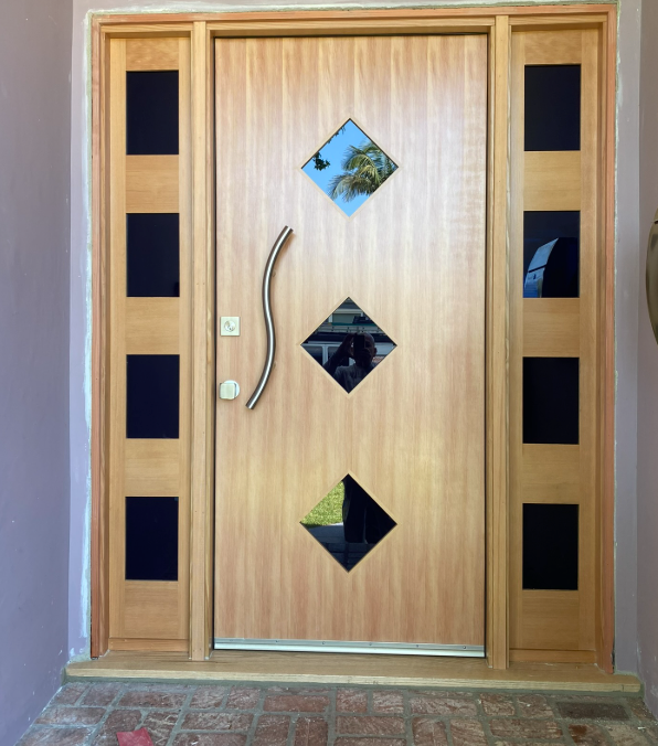 Wooden front door with diamond-shaped glass windows and black side panels.
