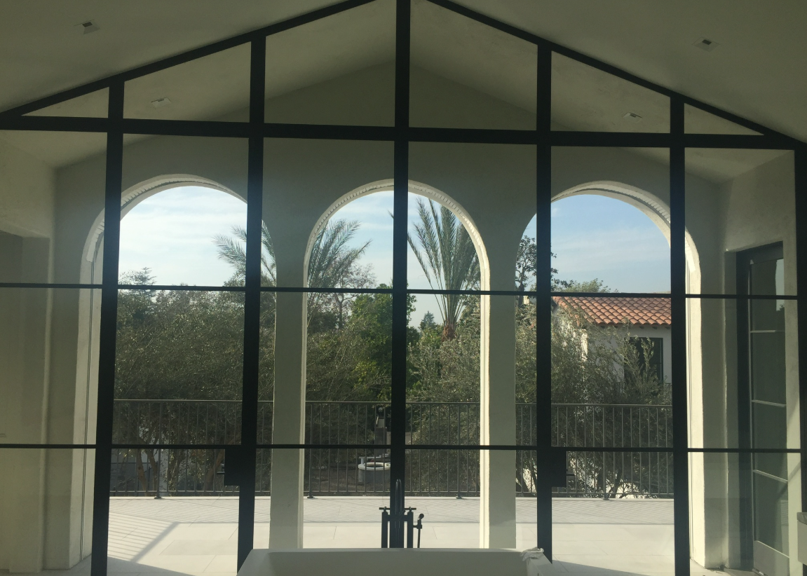 Open arched windows with white frames, overlooking greenery and a balcony.