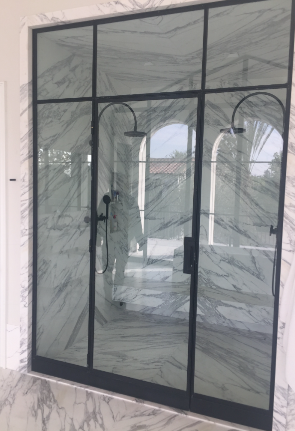 Black framed glass shower enclosure with marble walls and two shower heads.