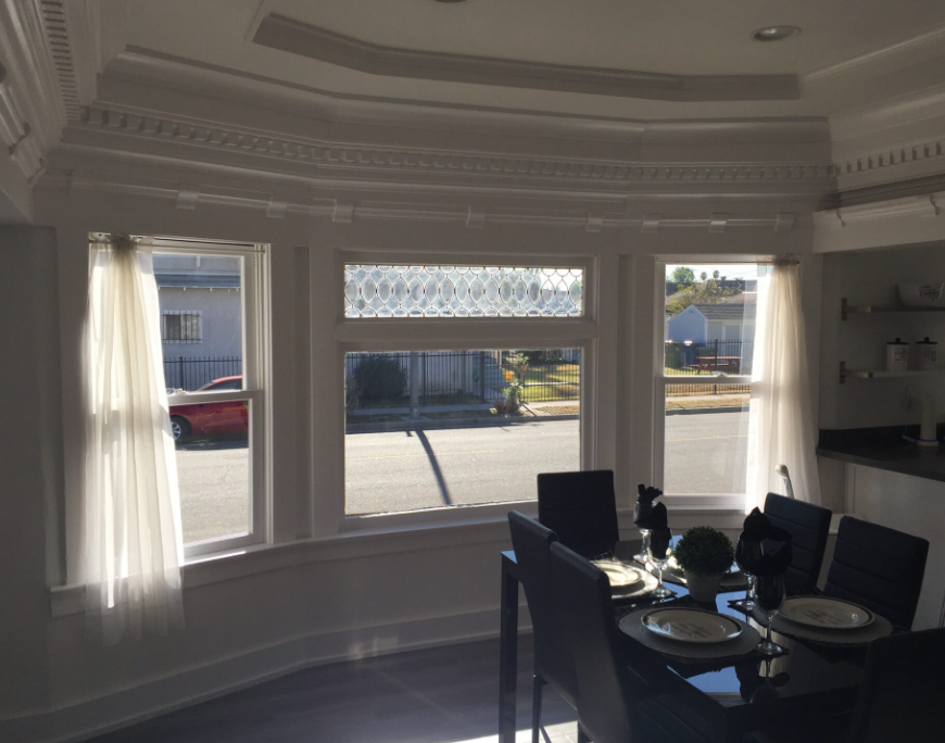 A dining room with a bay window, a table set for a meal, and sheer curtains.