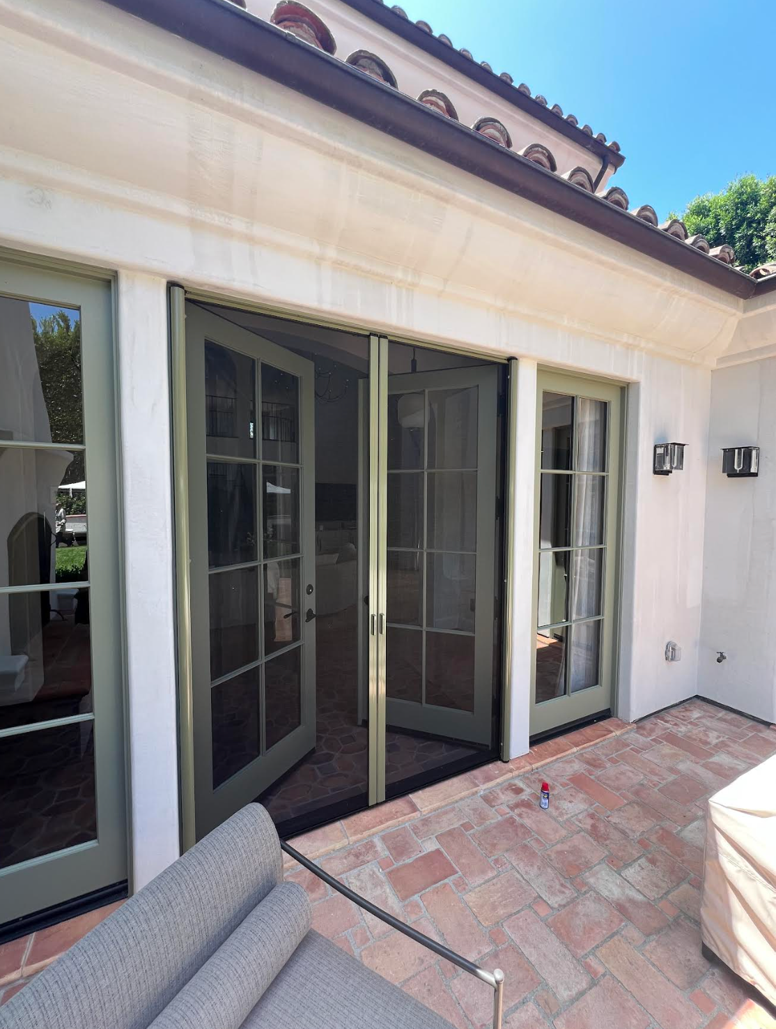 Outdoor patio doors with a screen, brick floor, and seating, painted in shades of green and white.