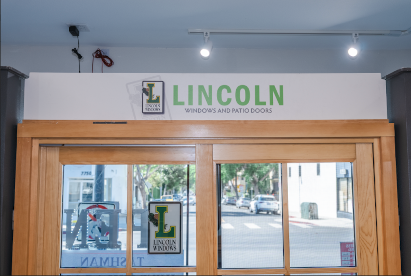 Sign for Lincoln Windows and Patio Doors above wooden-framed glass doors. Green and white logo and text.
