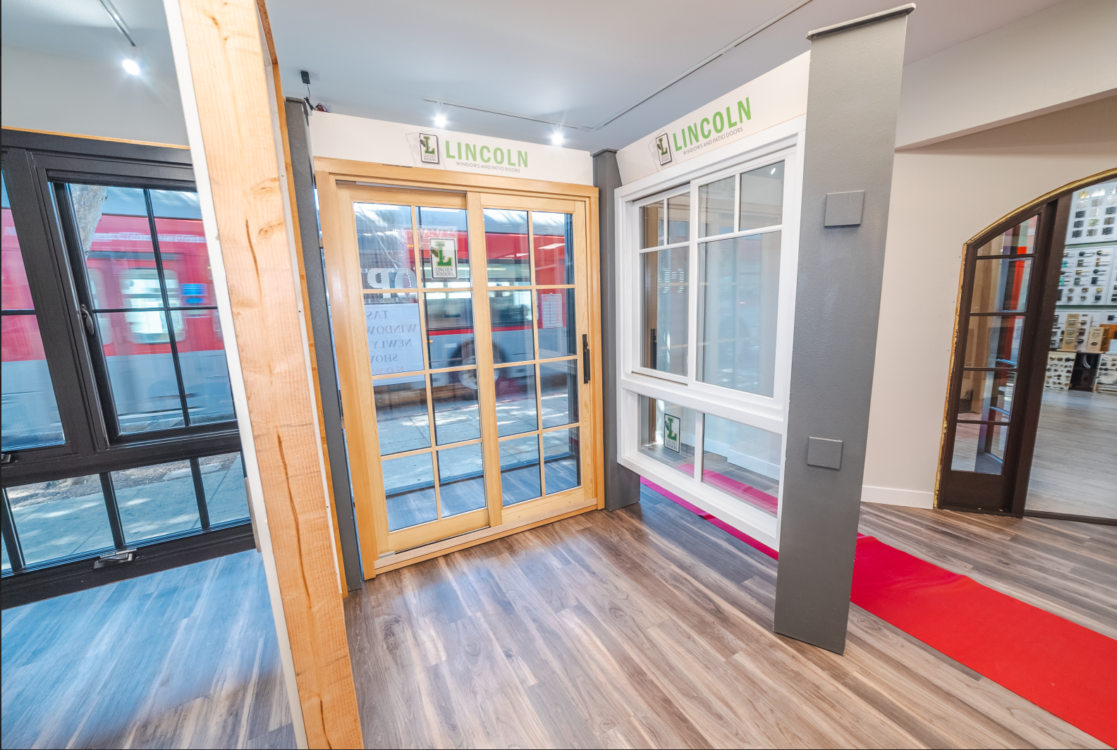 Window showroom with various display windows on gray and wooden floors. Red carpet leads to an arched doorway.