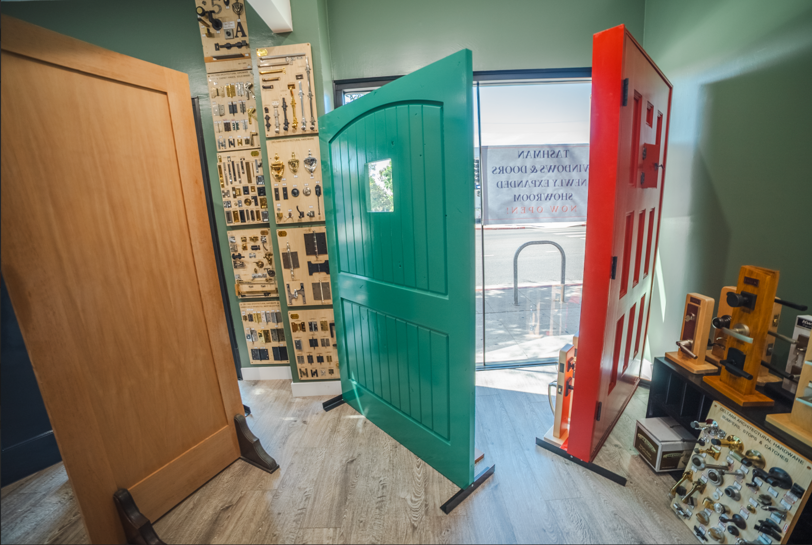 Three colorful doors displayed in a shop; a wooden door, a green door, and a red door.