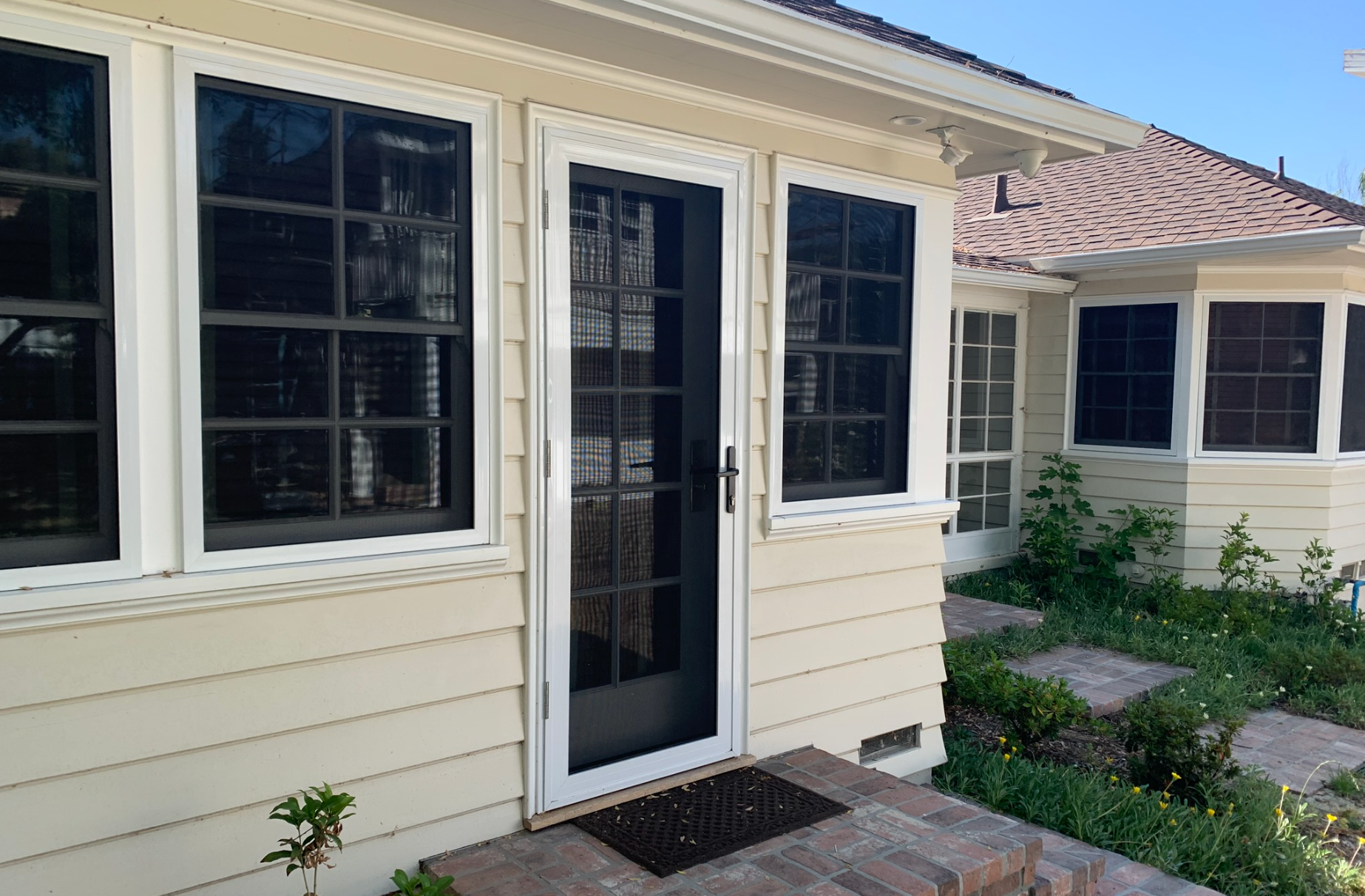 Window with burgundy trim reflecting trees, set in a yellow stucco wall.
