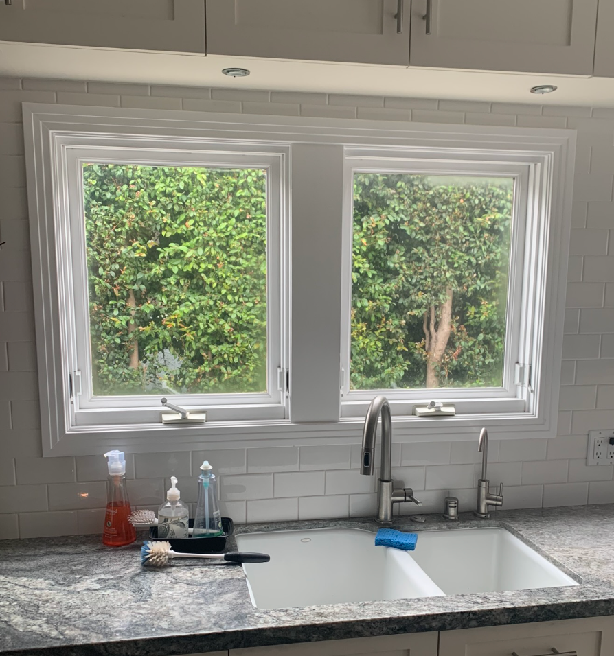 White kitchen windows with greenery view above a granite countertop with a sink and faucet.