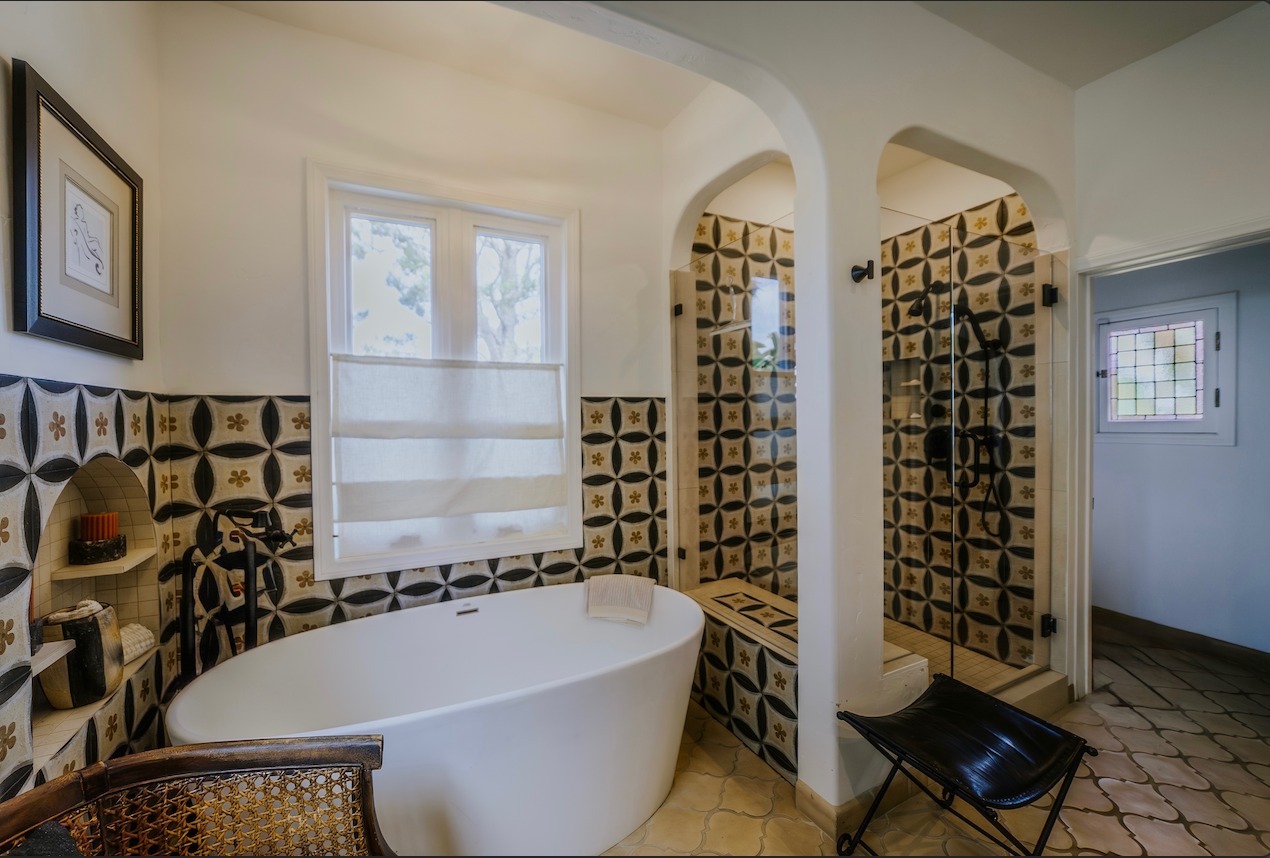 Bathroom with a white tub, patterned tile walls, and an arched shower entrance.