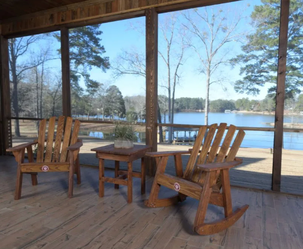 Two wooden chairs and a small table on a screened porch overlooking a lake.