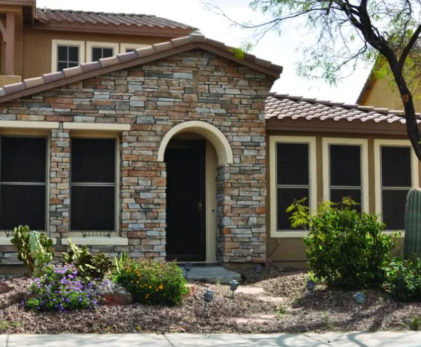 Stone-covered house with arched doorway and windows, surrounded by desert landscaping.