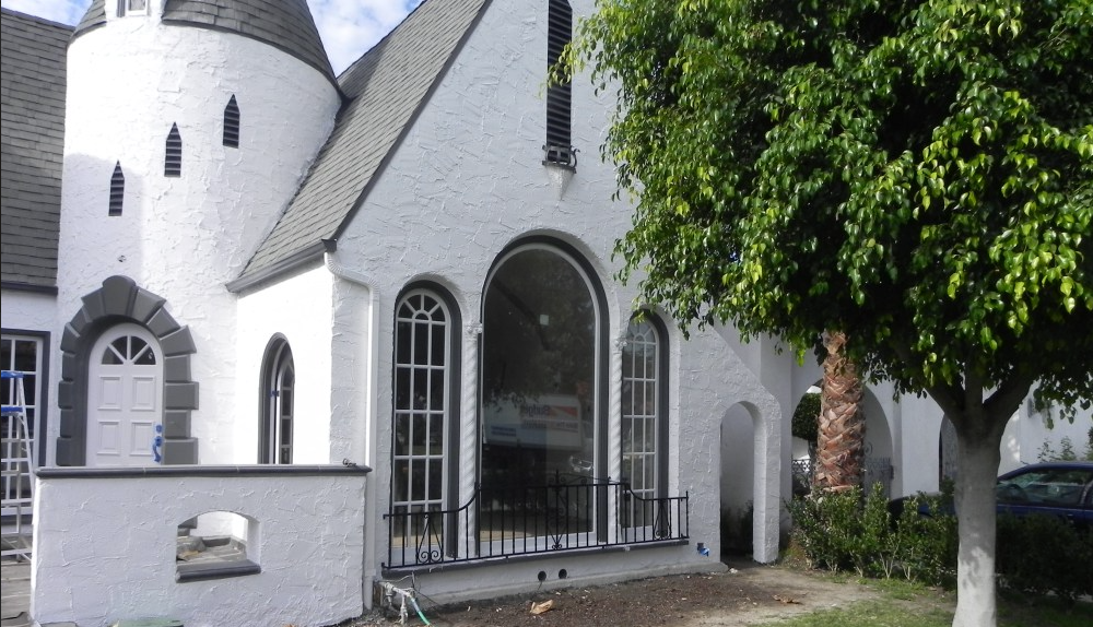 White stucco building with turret and arched window, black trim, and a tree.