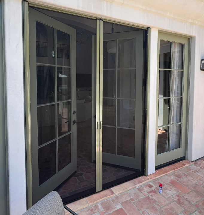 Green-framed French doors featuring a retractable mesh screen door installed on an outdoor patio.