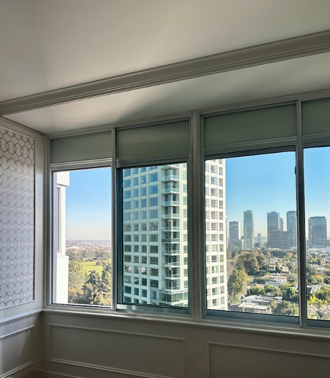 A view of a high-rise city skyline through a large, multi-paned window in a room with cream-colored paneled walls.
