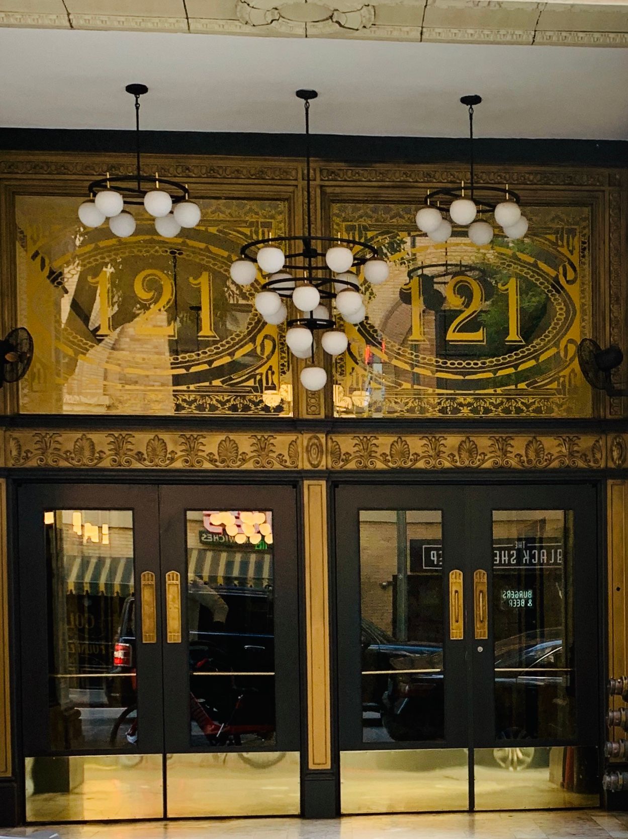 Entrance with black doors, gold trim, mosaic art, and globe chandeliers;