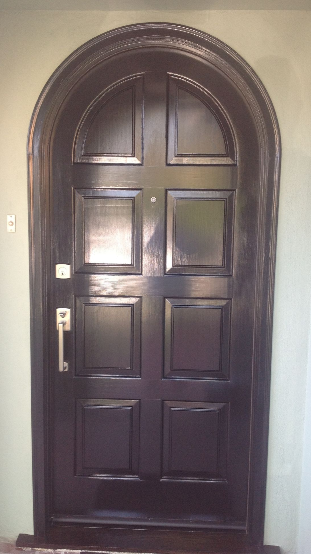 Black arched wooden door with paneling and silver handle.