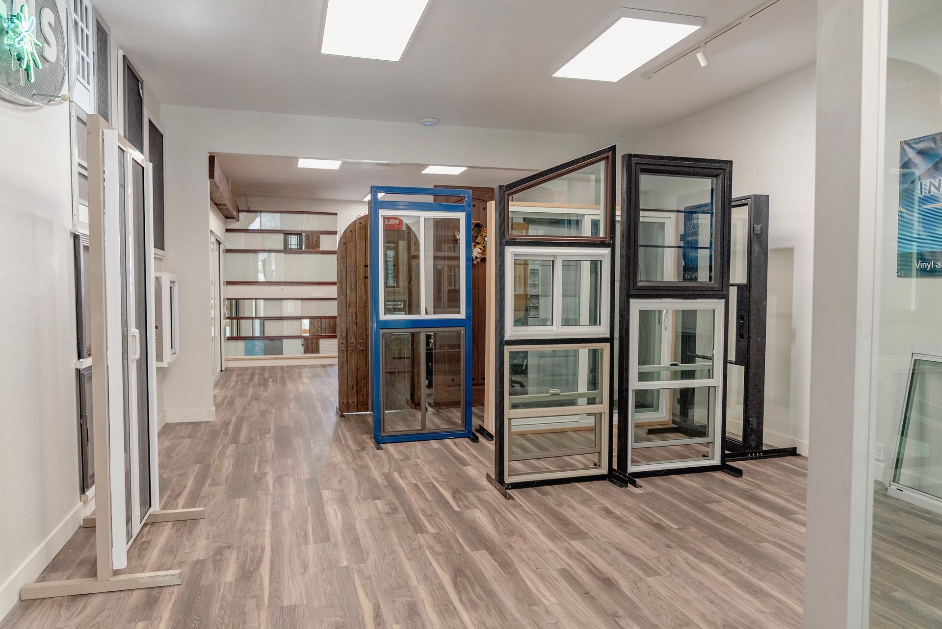 Showroom displaying window styles; various frames on stands, wood flooring, neutral walls.