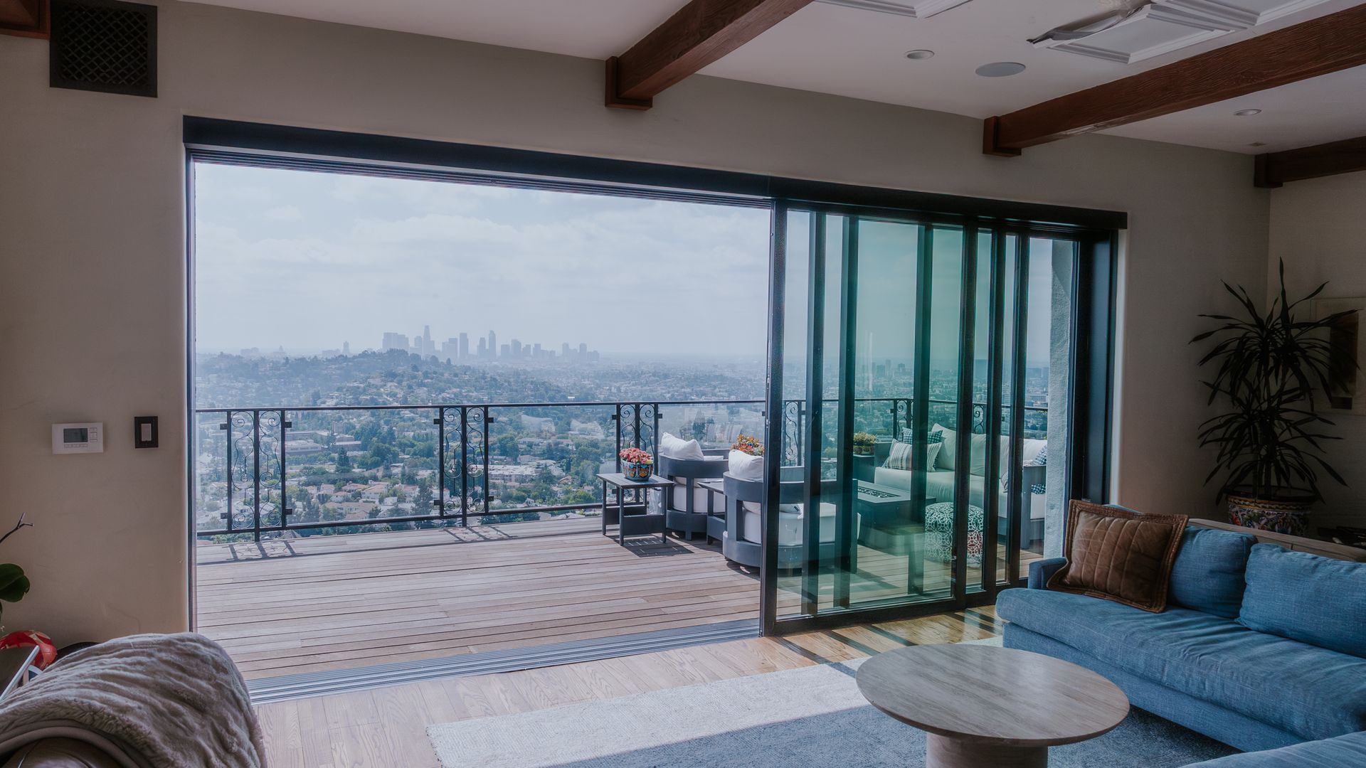Folding glass doors open to a patio with seating, revealing a living room with a chandelier.