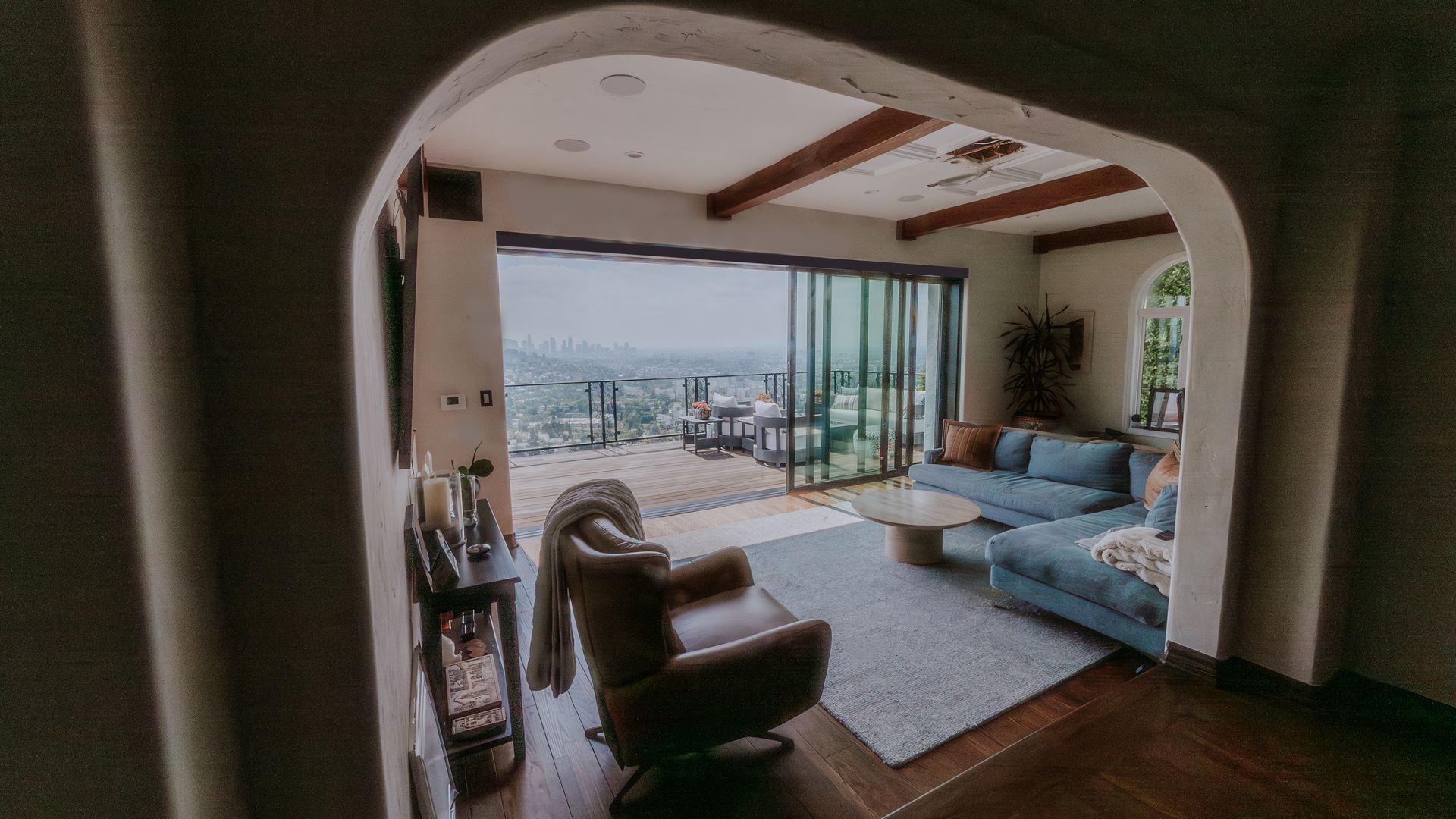 Open doors to a sunny city view. Interior with wood floors, white railings, and a cityscape in the distance.