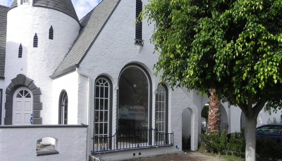 White castle-like building with arched windows and a turret; tree in the foreground.