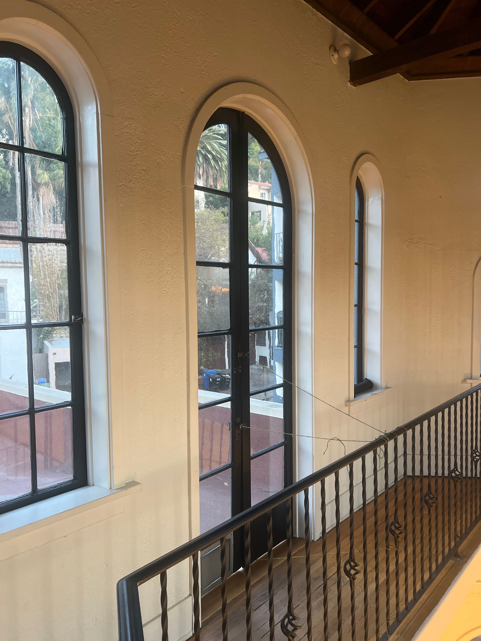 Window with burgundy trim reflecting trees, set in a yellow stucco wall.