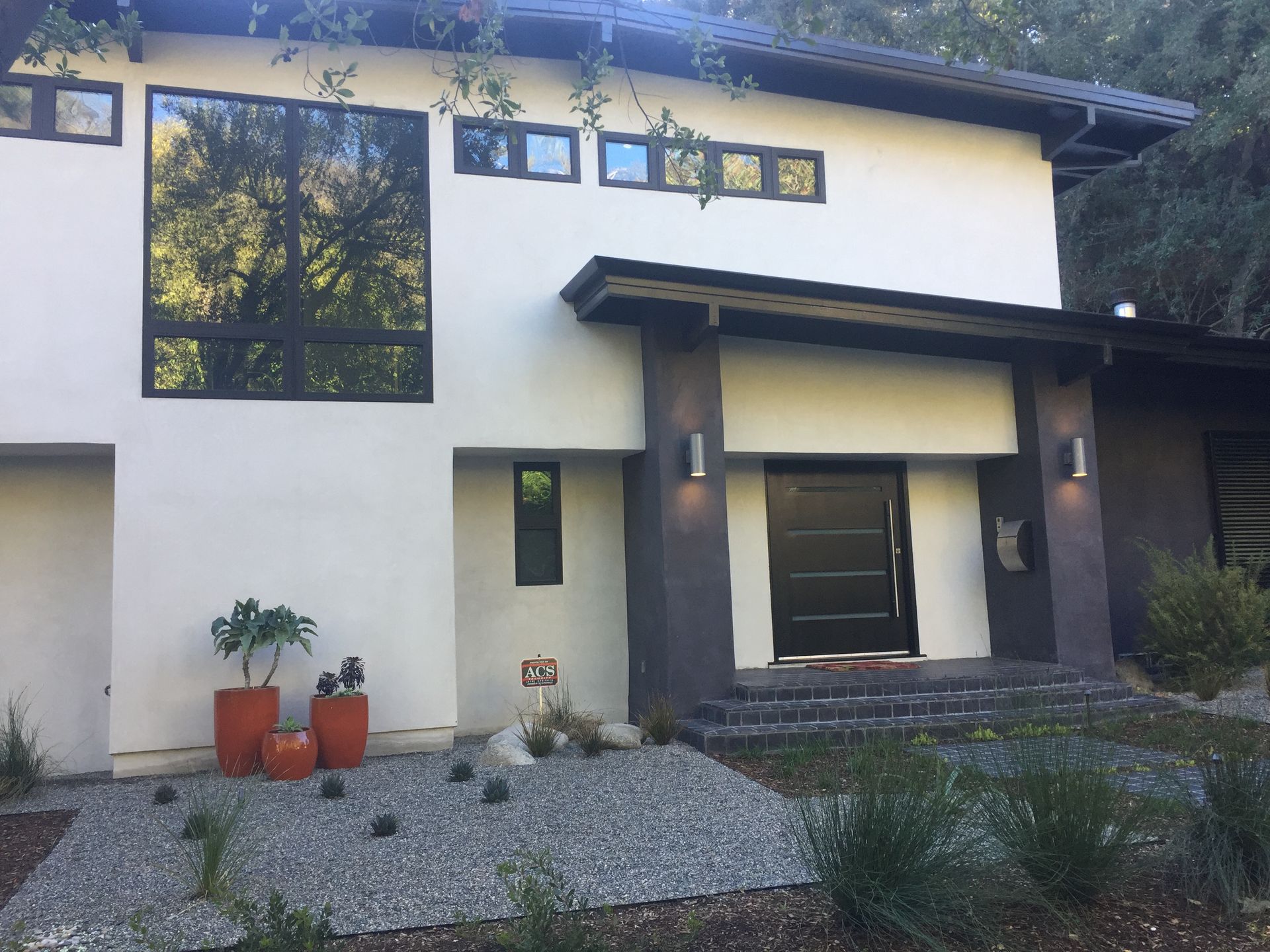 Modern home with large windows, black door, and orange planters.