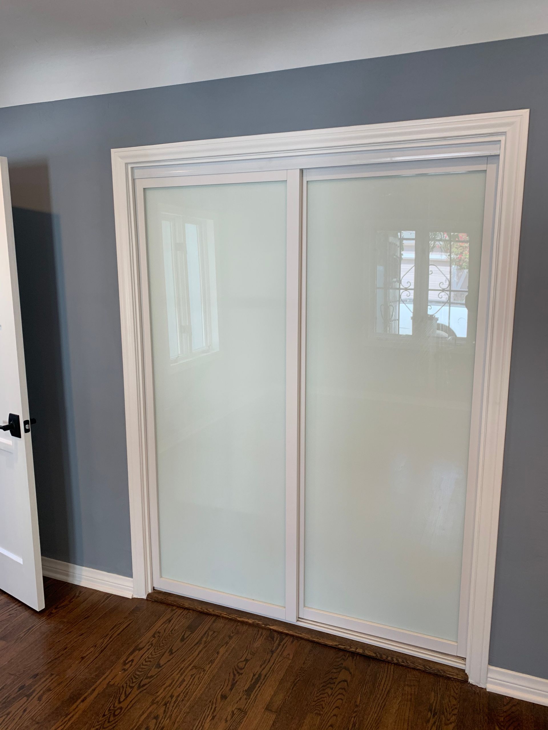 Sliding closet doors with frosted glass and white trim, set in a room with gray walls and a wooden floor.