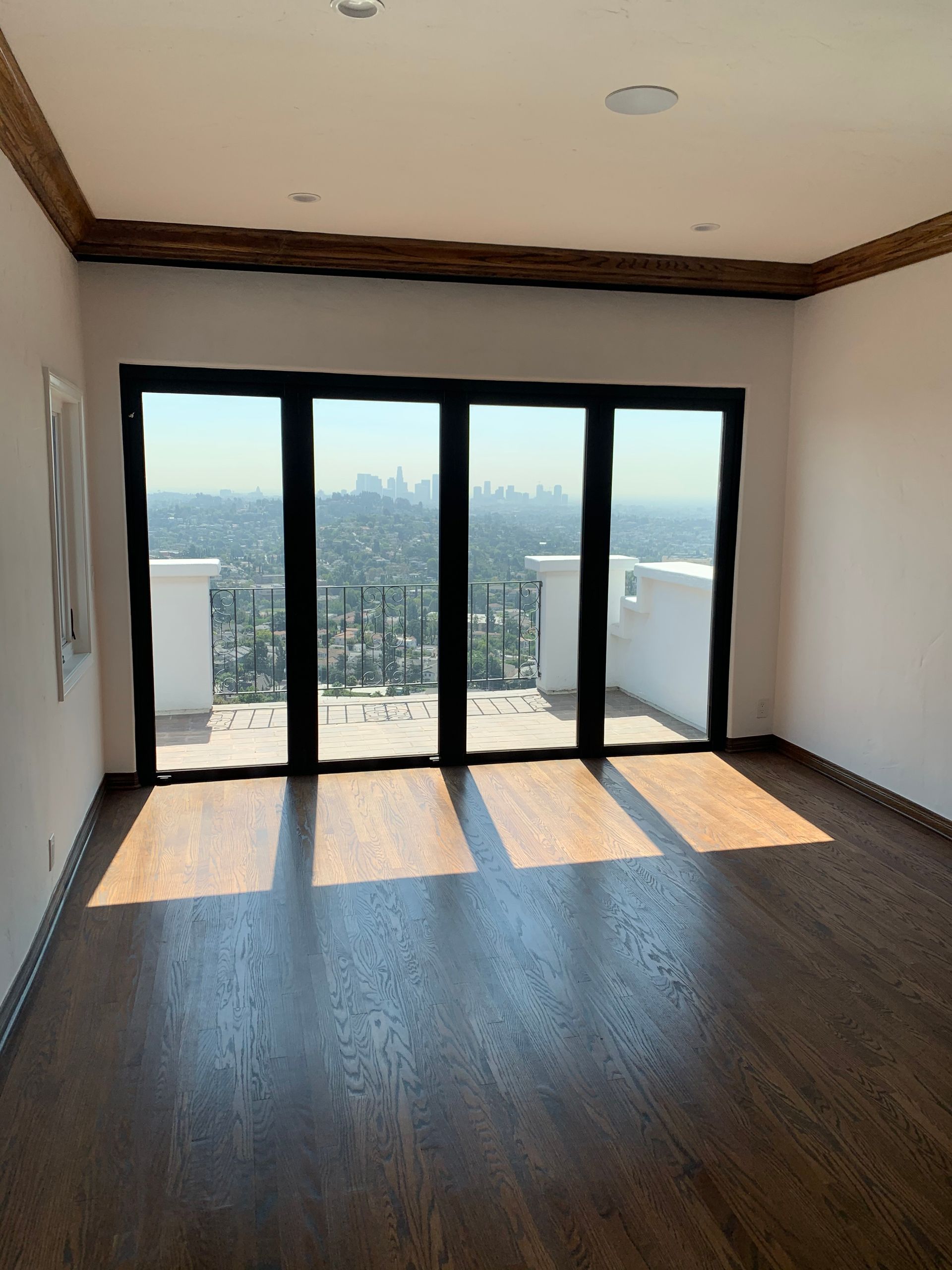 Bright room with large glass doors opening to a city view and balcony. Wooden floors.