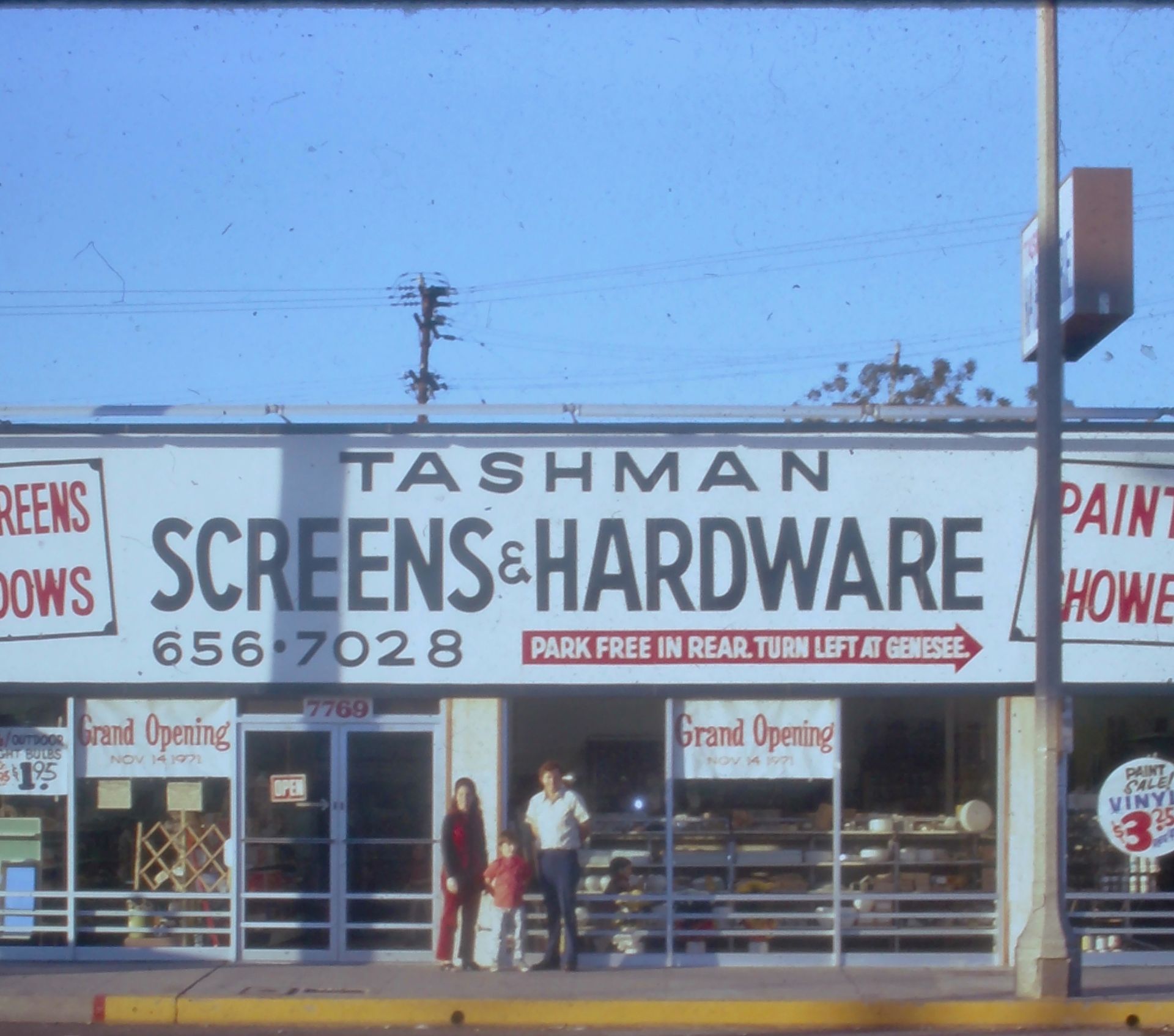 Elderly man in blue sweater and cap stands inside a store, a shelf of cleaning supplies to the right.