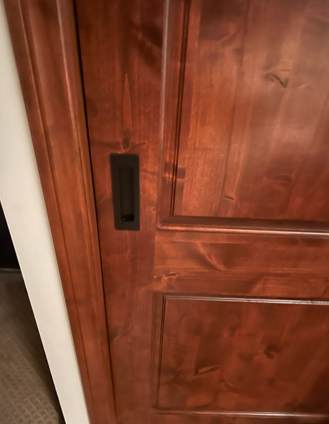Close-up of a stained wooden door with a recessed black handle, set in a white door frame.