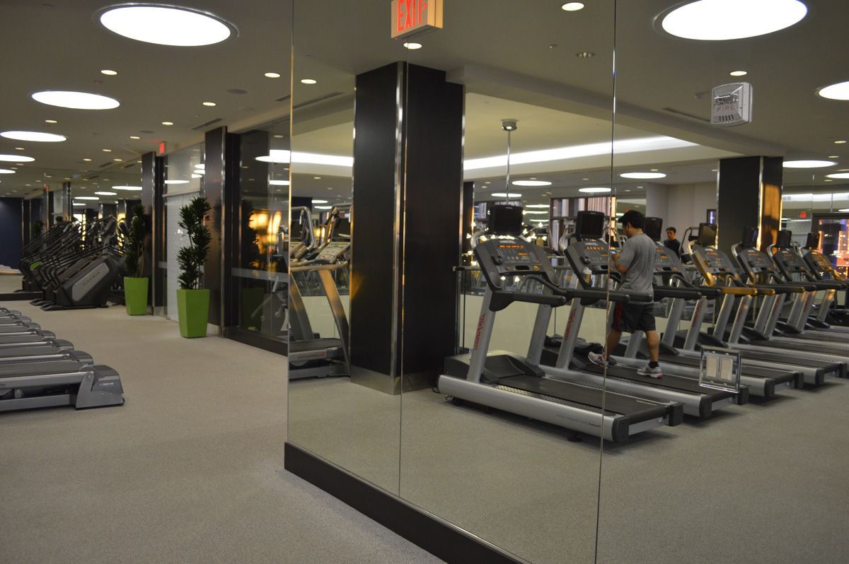 A well-lit gym with treadmills, elliptical machines, and mirrors. A person is on a treadmill.