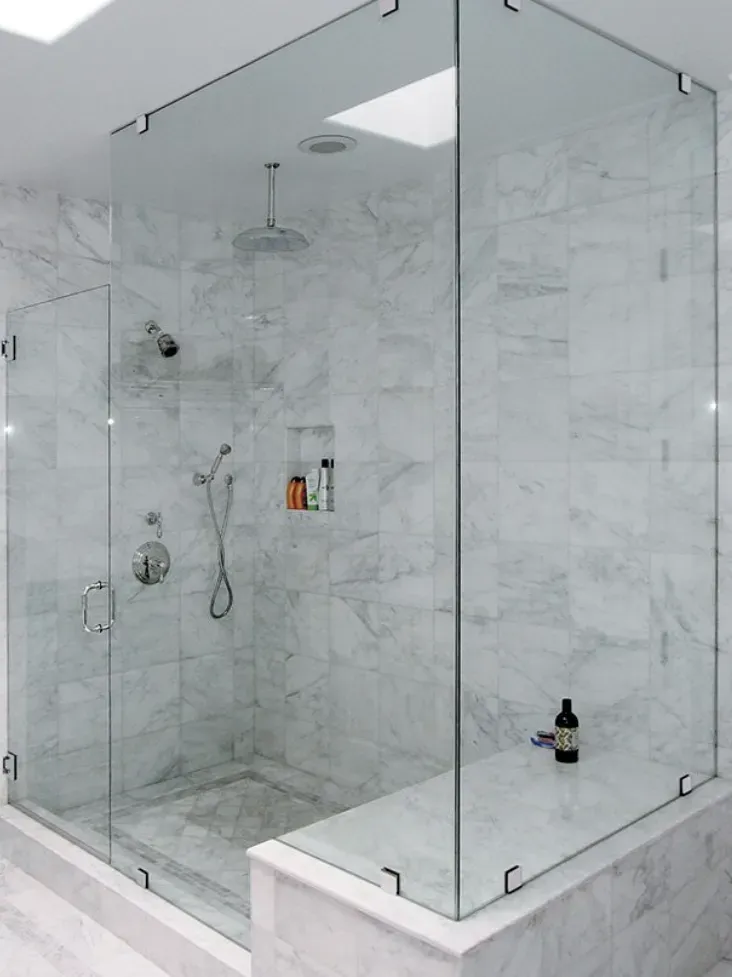 Glass shower enclosure with marble walls and bench.