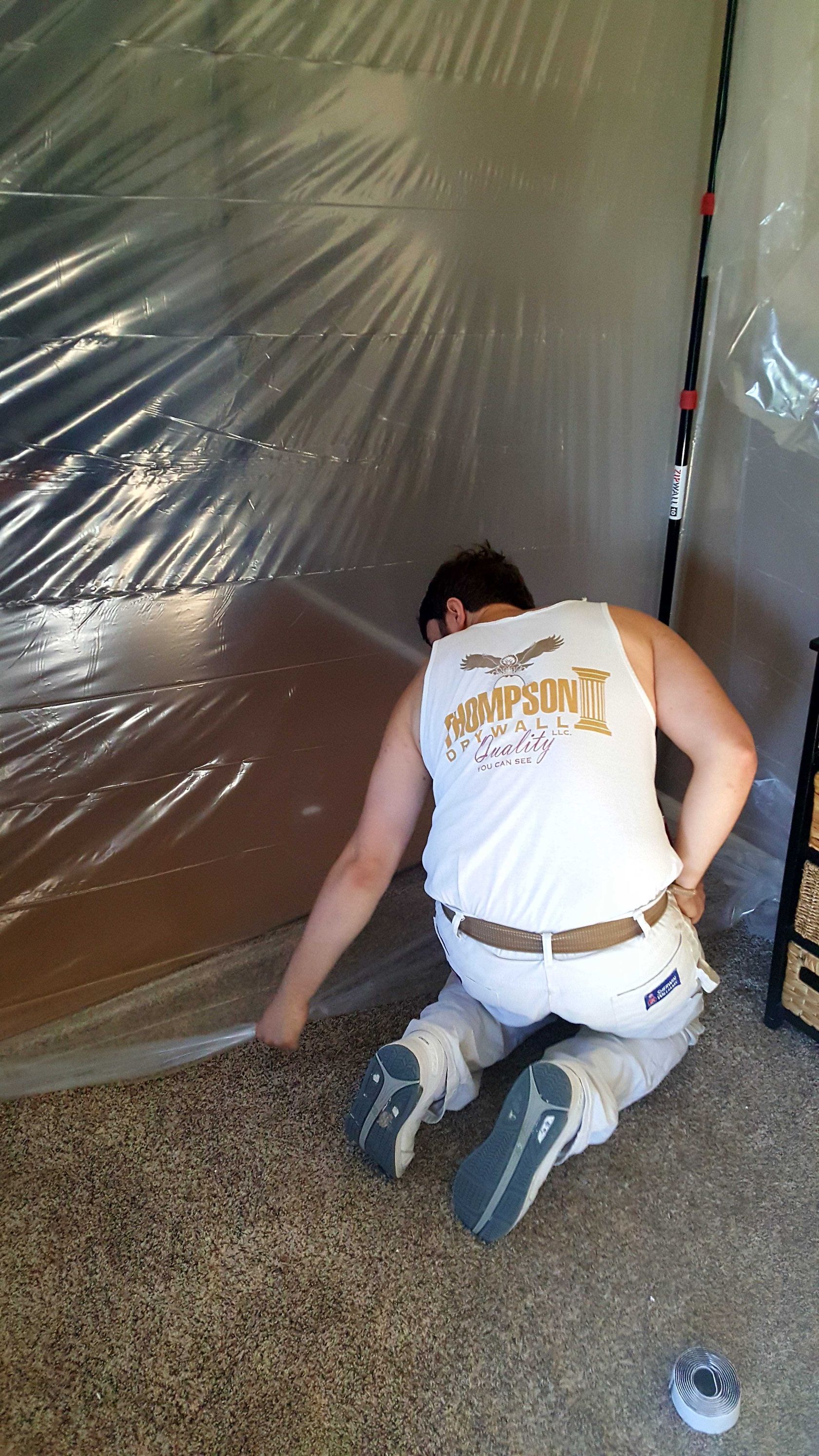 A man is kneeling on the floor under a plastic sheet.