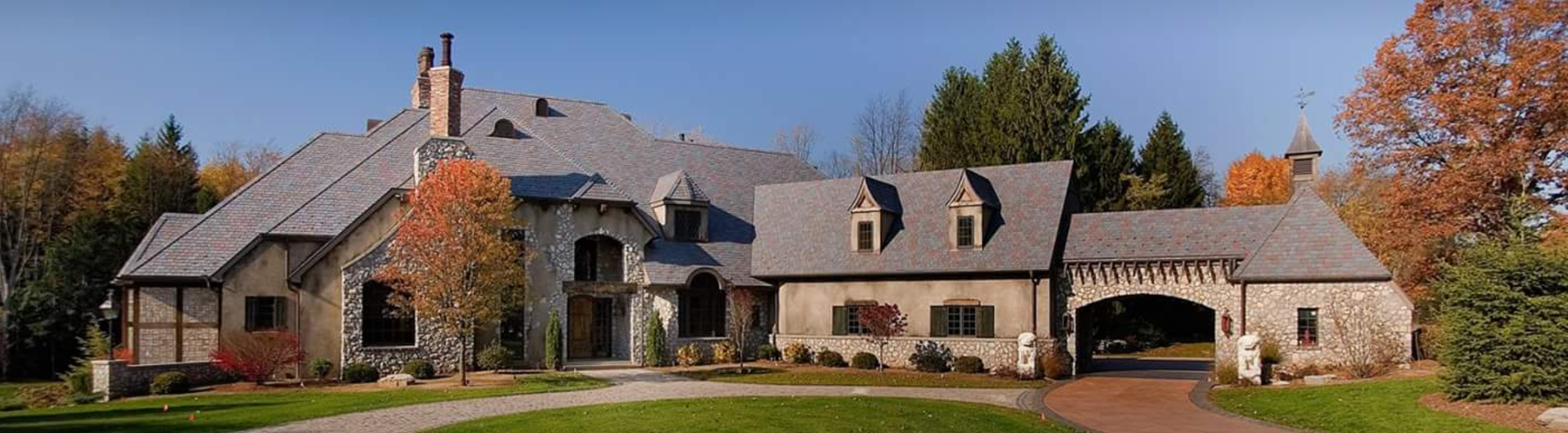 A large house with a driveway leading to it is surrounded by trees.