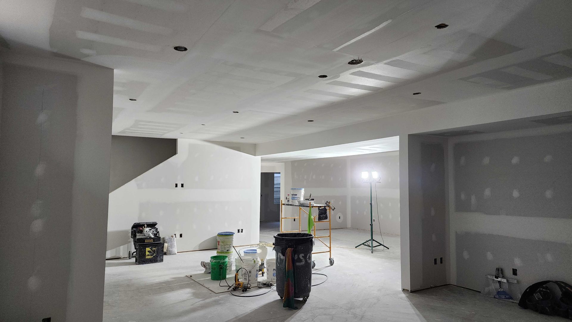 A large room with drywall walls and a trash can in the middle of it.