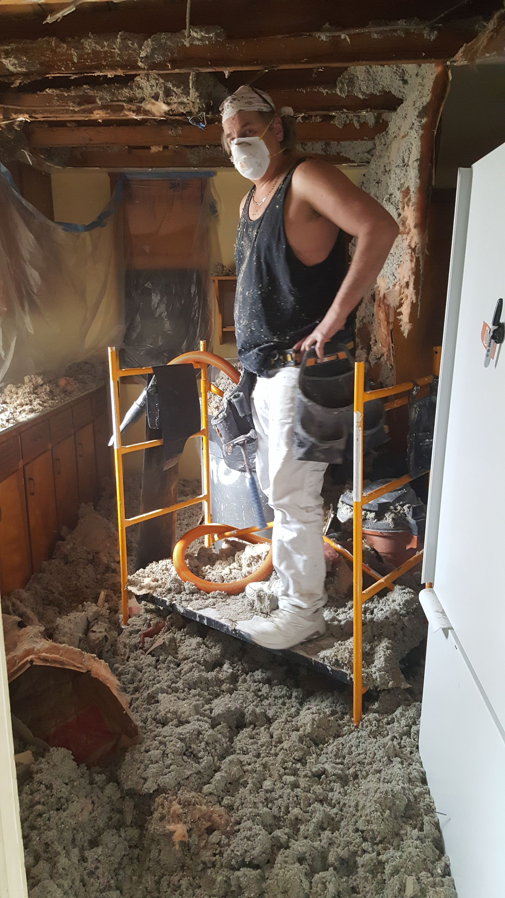 A man wearing a mask is standing on a scaffolding in a room.
