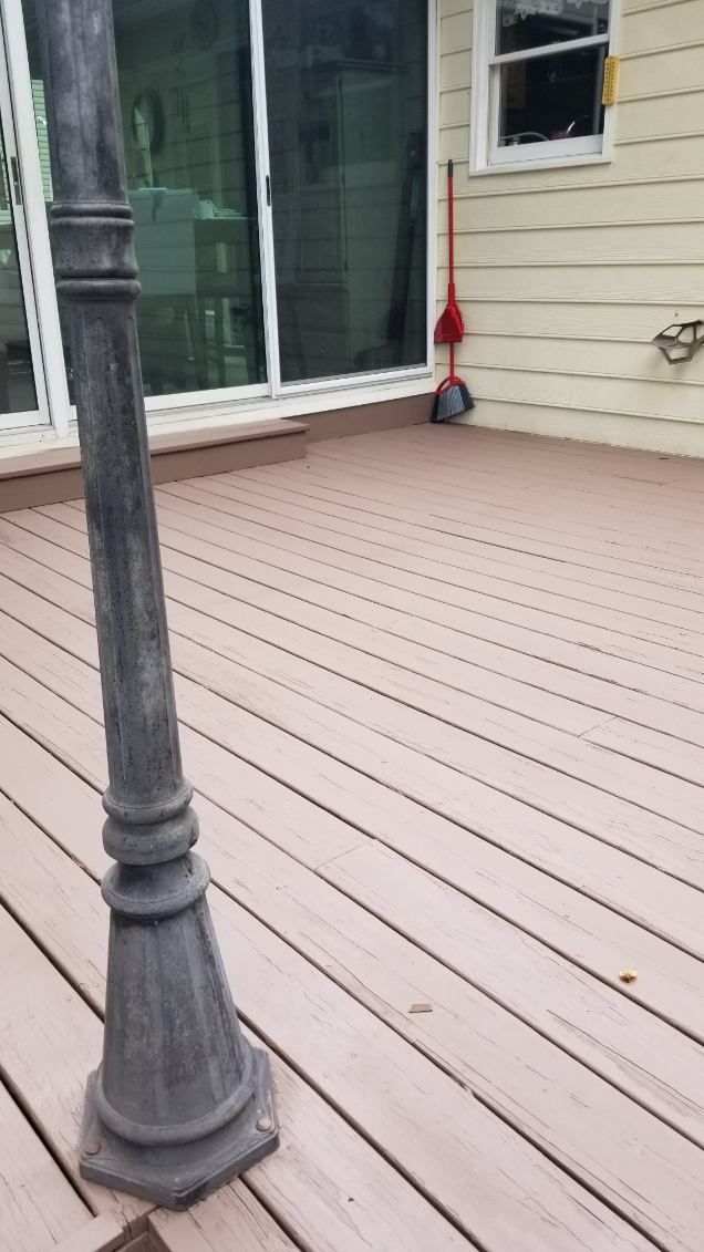 Wooden deck with a lamppost in the foreground, sliding glass door and broom against a beige wall in the background.