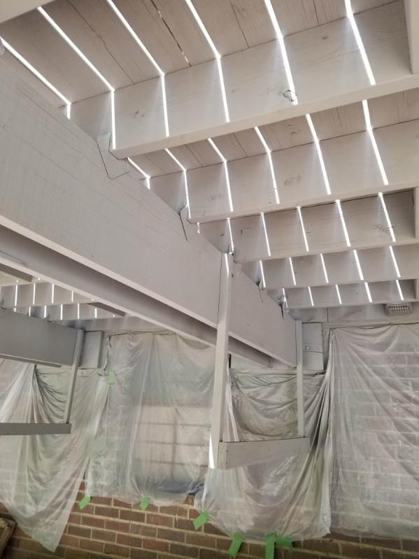 White-painted deck underside with exposed beams and joists. Plastic sheeting drapes from the structure. Brick wall visible.