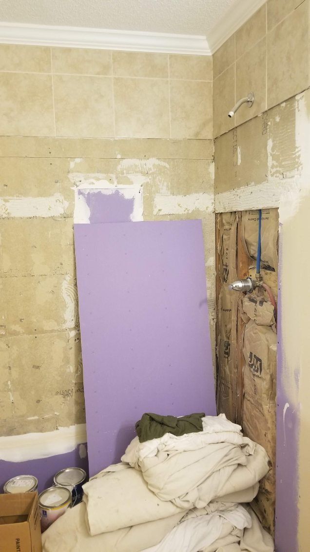 Bathroom remodel in progress; purple drywall leaning against damaged wall. White towels and a box are on the floor.