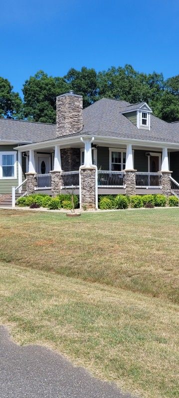 Green house with stone chimney and porch under a clear, blue sky.
