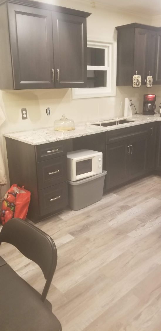 Kitchen with dark cabinets, white countertop, microwave, and gray storage bin.