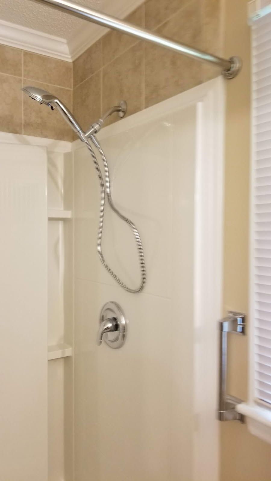 Shower stall with a chrome shower head, fixtures, and grab bar.
