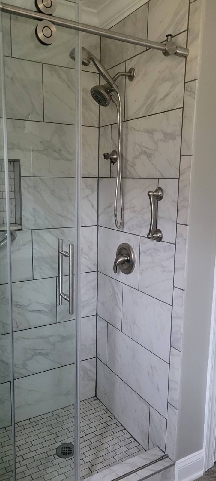 A modern marble-tiled shower with a sliding glass door and chrome fixtures.