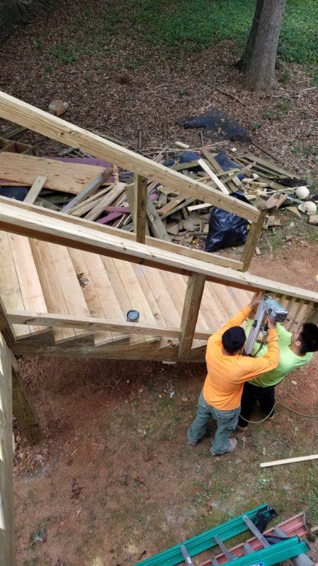 Two construction workers building outdoor wooden stairs, one using a nail gun.