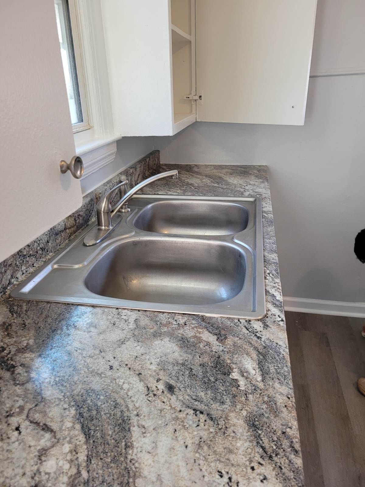 Kitchen sink with stainless steel basins on a marbled countertop, with cabinets above.