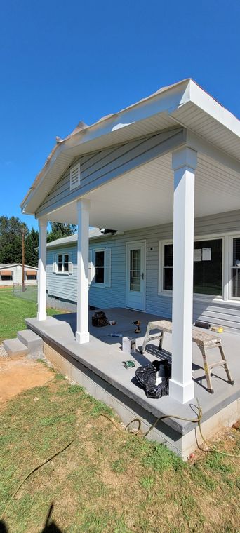 House with a porch under construction; blue siding, white trim, and a concrete patio.