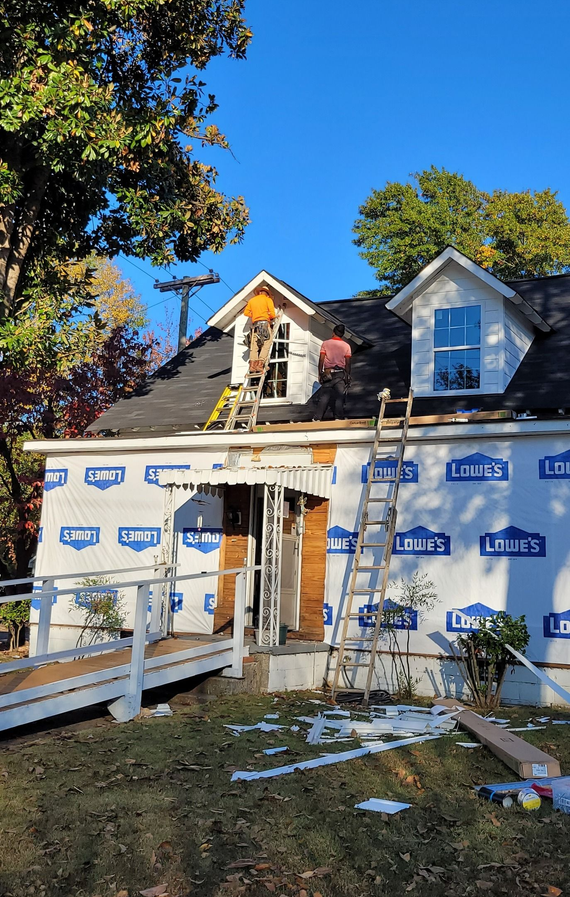 House under construction; blue Lowe's wrap, scaffolding, ladder, exposed framing, and dormers.