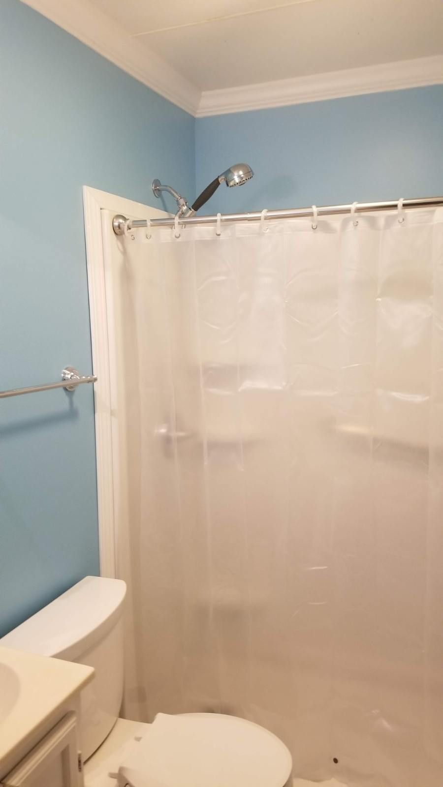 A bathroom with a clear shower curtain, toilet, blue walls, and a silver shower head.