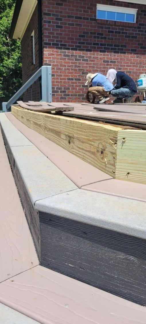 Workers on a deck with brick building in the background. Construction in progress. Wooden structure with composite edging.