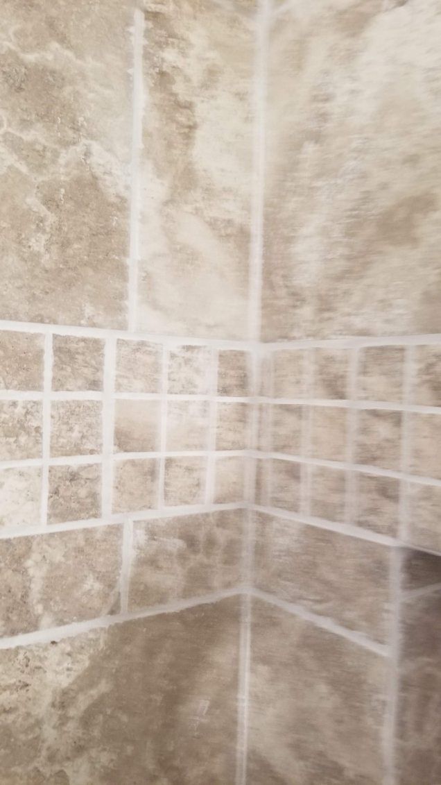 Corner of a shower with marbled beige tiles and a border of small square tiles.