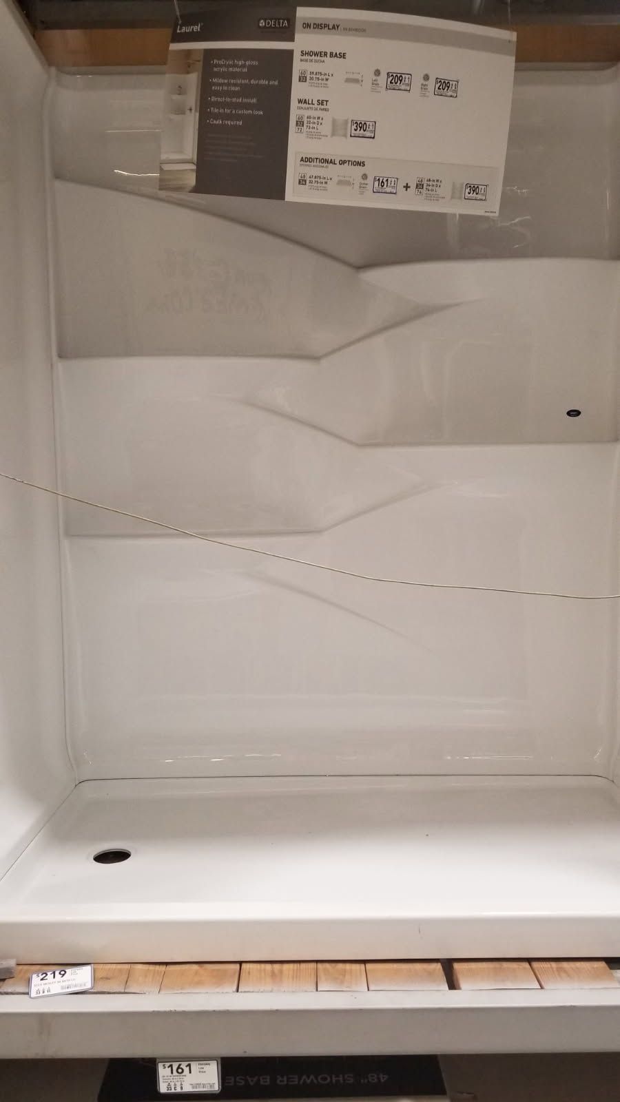 White shower stall with three ledges, drain, and price tag.